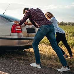 A man and woman pushing their car that has broken down..