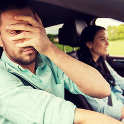 A male passenger in a car covering his eyes because he's afraid of what he sees.