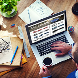 A man, sitting at a desk, shopping online for the best price for a car rental.