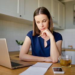 A woman deep in thought sitting at her desk looking over her computer screen.