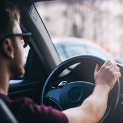 A young man behind the wheel of his car driving.